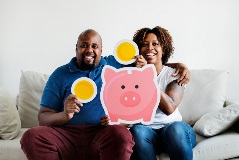Smiling couple with cutout of piggy bank and coins.