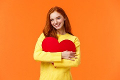 Woman with cut out heart against plain background.